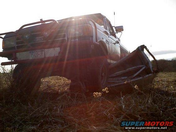 1995 Ford F-150 with custom front bumper and damaged bed, parked in a field