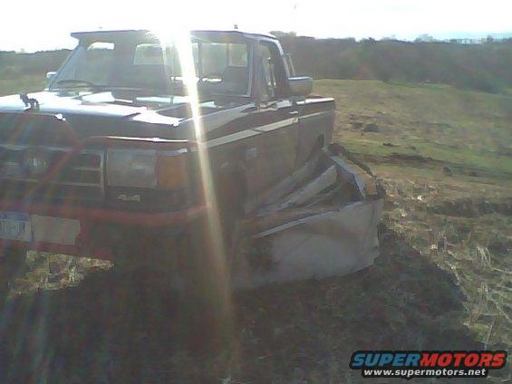 Dark blue Ford F-150 with a damaged front fender and aftermarket bumper, parked on a grassy incline