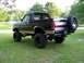 1990 Ford Bronco - This lifted 1990 Ford Bronco is parked on a grassy lawn with trees and a pool in the background.