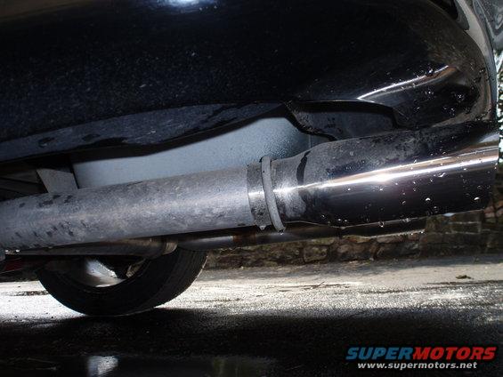 Close-up of a shiny exhaust tip and pipe, with a tire visible below