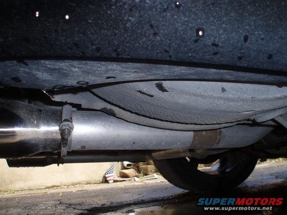 Underside view of a car's exhaust pipe and undercarriage, showing a tire on the right