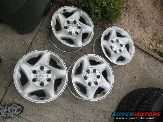 Four silver alloy wheels with five spokes and Toyota logos, resting on concrete