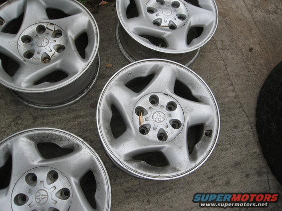 Four silver Toyota wheels with five spokes each, sitting on concrete