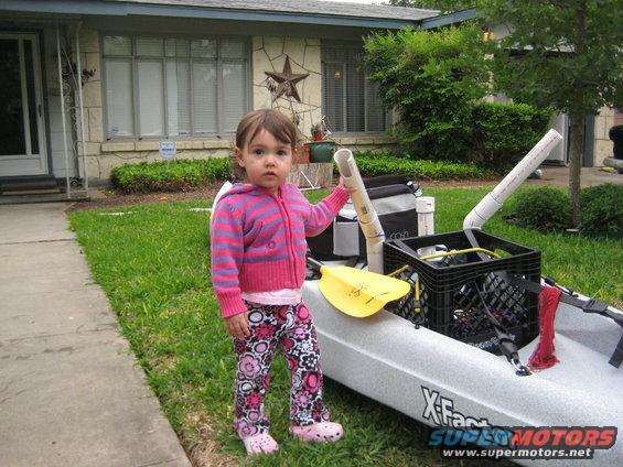 Child standing next to a kayak with PVC pipe attachments