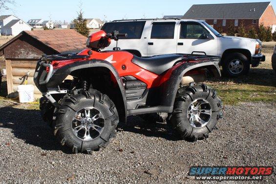 Red ATV parked on asphalt in front of a white SUV and a building