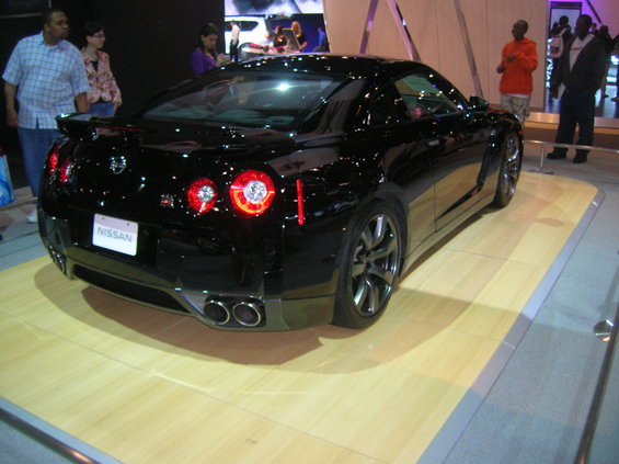 Black Nissan GT-R parked on display platform, rear view showing taillights and exhaust
