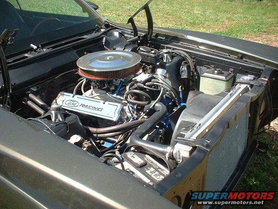 Ford V8 engine with Ford Racing valve covers and aftermarket air cleaner. Battery and radiator visible