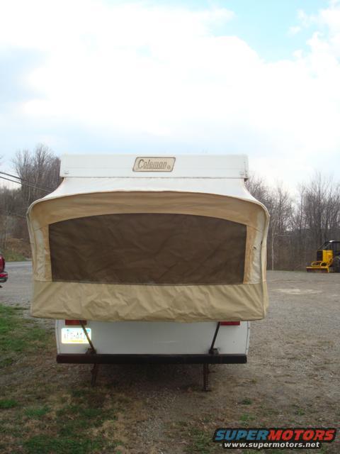 Rear view of a white pop-up camper with a tan canvas tent and a Coleman logo
