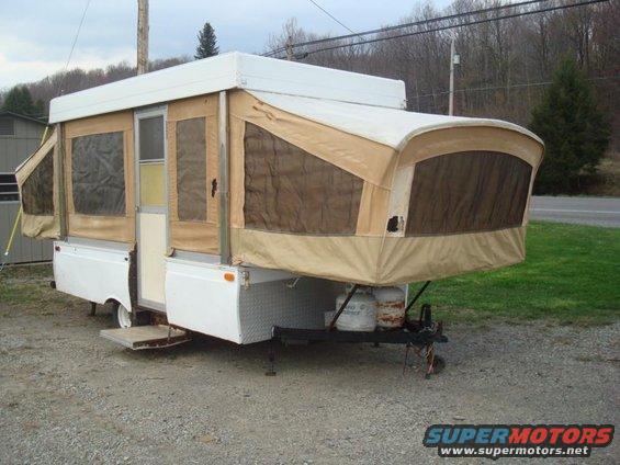 Pop-up camper trailer with tan canvas sides and white body, parked on gravel