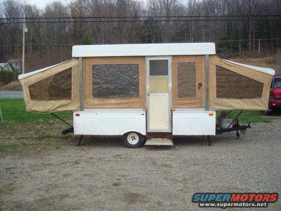 Pop-up camper with tan canvas sides and white body, parked on gravel