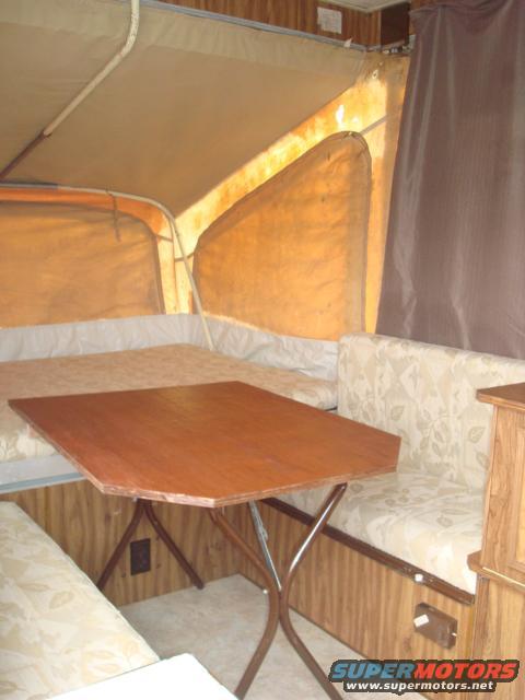 Interior of a pop-up camper with a wooden table, beige seating, and tan canvas walls