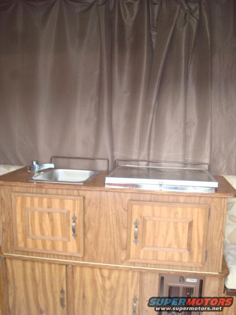 Camper interior with sink, stove, and wood cabinets