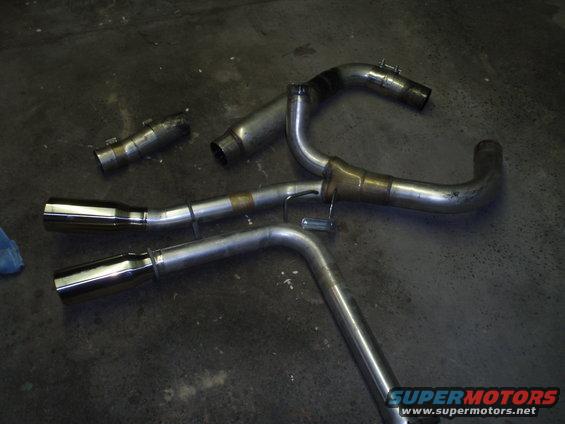 Several pieces of polished and unpolished exhaust piping, including mufflers and bends, laid out on a concrete floor
