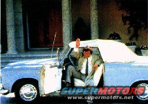 guy in suit waving from inside a light blue convertible with a white top