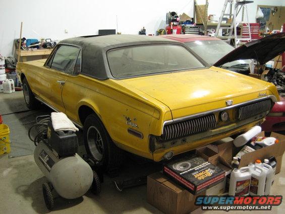 Yellow 1968 Mercury Cougar coupe with a black vinyl top, seen from the rear three-quarter angle in a garage