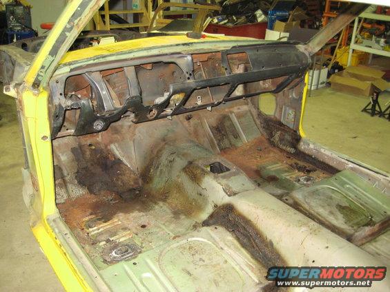Interior of a car undergoing restoration, showing a stripped dashboard and rusty floor pans