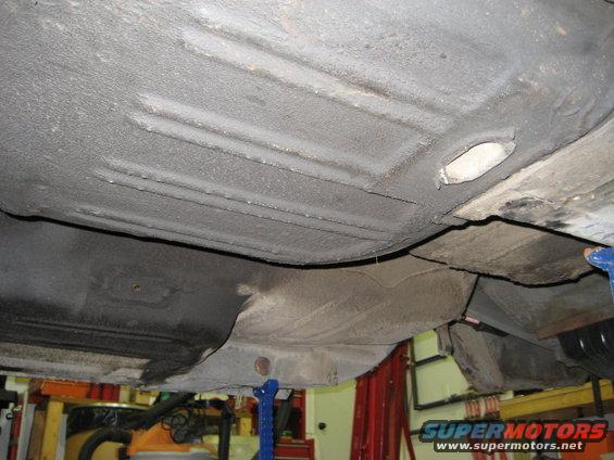 Underside of a vehicle on jack stands, showing the floor pan and frame rails with some surface rust