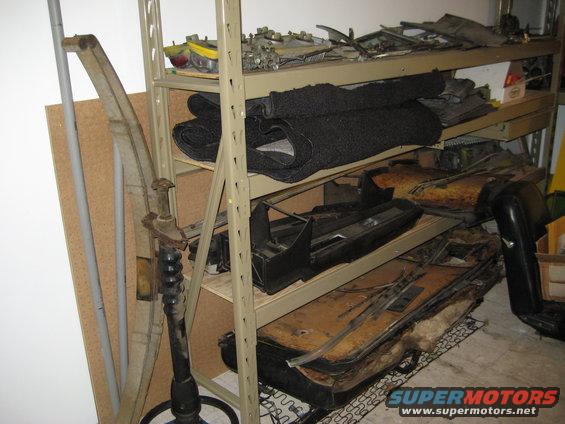 Shelving unit holding car parts like seats, carpet, and engine components