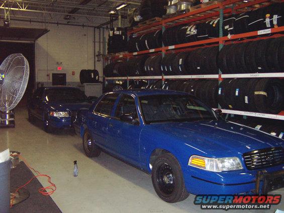 Two blue sedans parked inside a garage with shelves of tires in the background