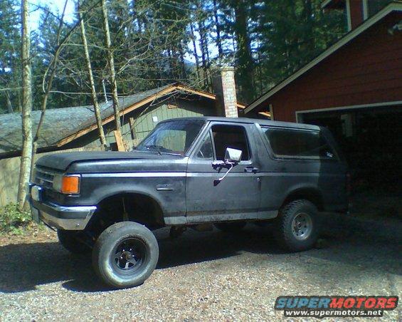 1987 Ford Bronco parked in gravel driveway next to a red garage