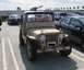1990 Ford Bronco - A tan jeep, possibly a military surplus vehicle, is parked in a lot with other cars under a partly cloudy sky.