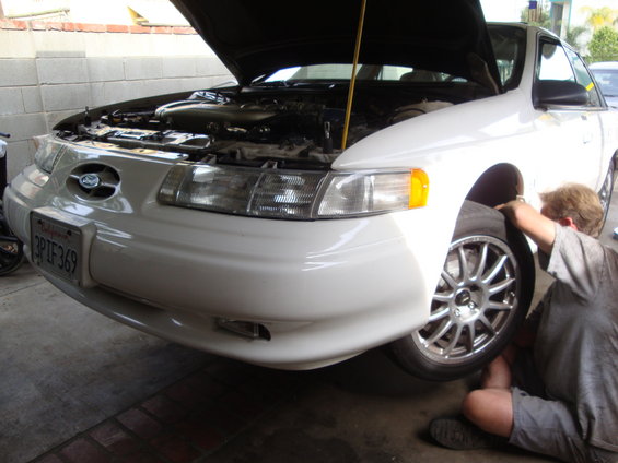 1995 Ford Taurus with hood up, someone working on front wheel