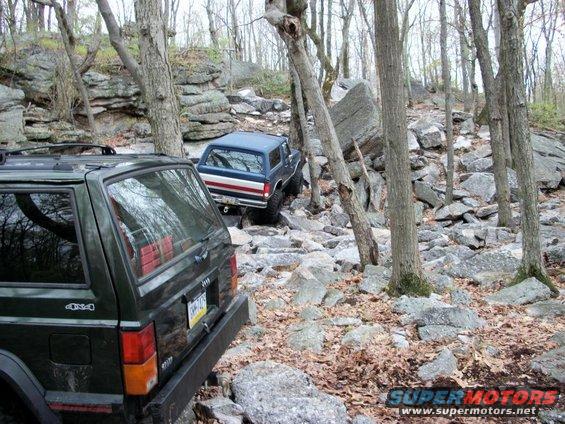 Blue 1987 Ford Bronco with red and white side stripes navigating a rocky trail
