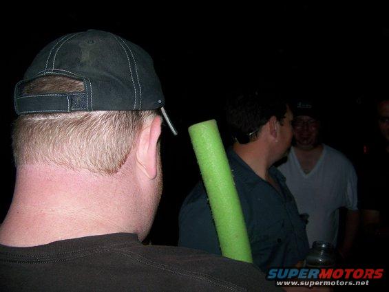 People gathered at night, one person holds a green foam tube