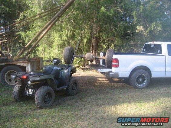 ATV next to a pickup truck with an axle and spare tire being loaded