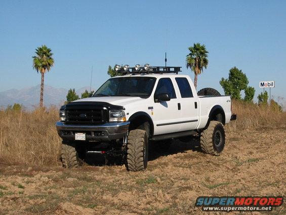 White pickup truck with big tires and roof lights parked off-road