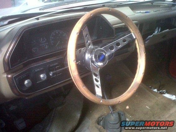 Interior shot of a vehicle showing a wood-rimmed steering wheel and dashboard