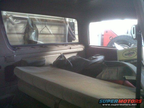 Interior view of a vehicle, showing seats, stored items, and a spare tire visible through a side window