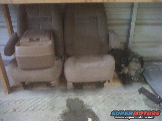 Two tan car seats and a transmission are on display in a garage