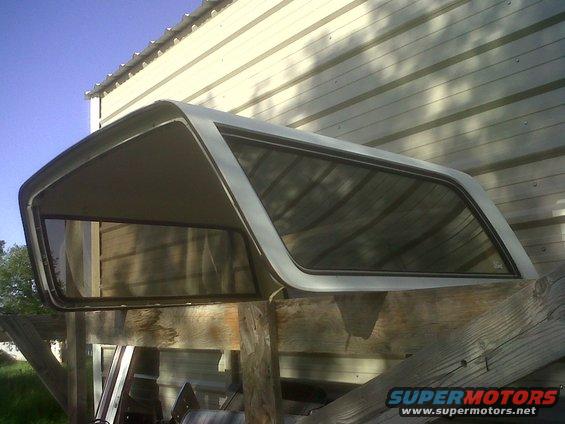 Truck cap with tinted windows, resting on wooden beams. Building in background