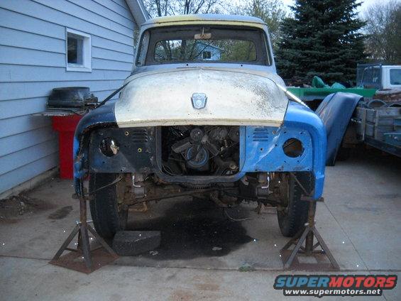 Front view of a disassembled 1953 Ford F-100 truck on jack stands, with engine exposed