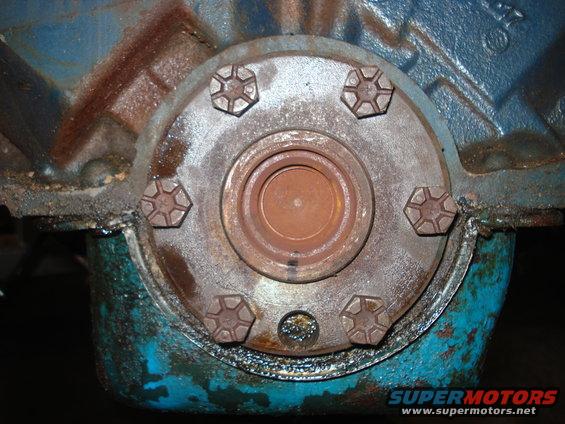 Close-up of a rusty metal flange with six bolts on a blue engine block