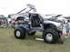 1994 Ford Bronco - This heavily modified pickup truck features massive tires and a lifted chassis, displayed outdoors with people and tents in the background.