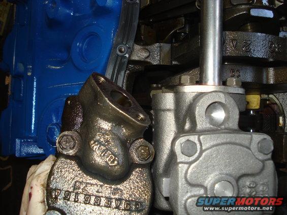 Close-up of engine parts, including a blue block and metal components. Part numbers are visible on one piece