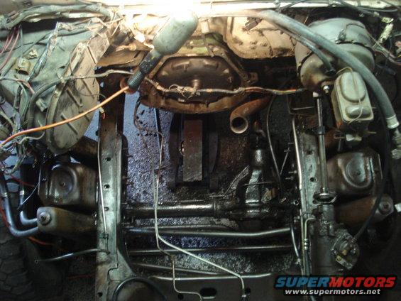 Engine bay and chassis of a vehicle, showing transmission, exhaust, and steering components. Appears dirty and under repair