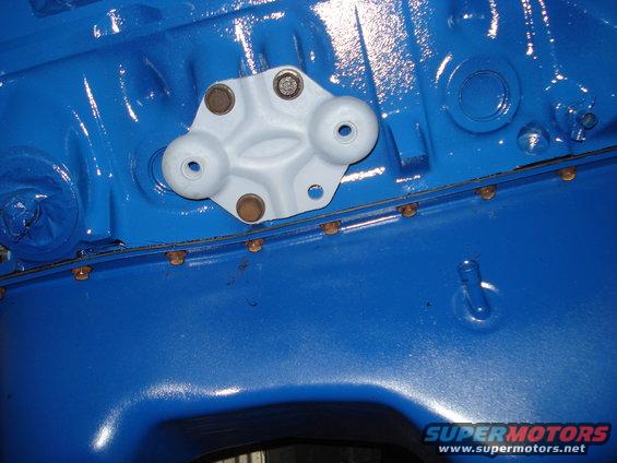 Close-up of a light gray bracket bolted to a bright blue engine block