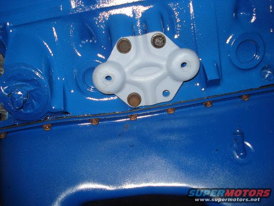 Close-up of a light gray bracket bolted to a bright blue engine block