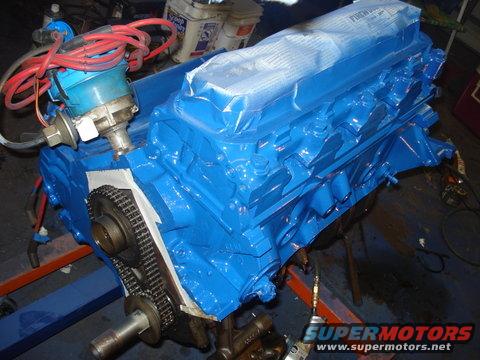 Blue engine block with distributor and red spark plug wires. Timing chain and gears visible on the side