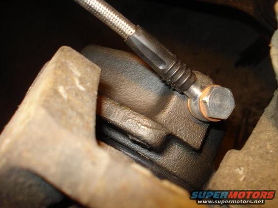 Close-up of a vehicle's brake caliper with a braided metal brake hose attached