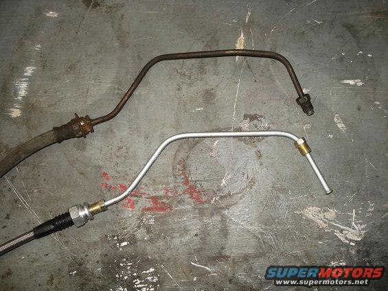 Two brake lines on a gray surface; one is rusty metal, the other is new aluminum
