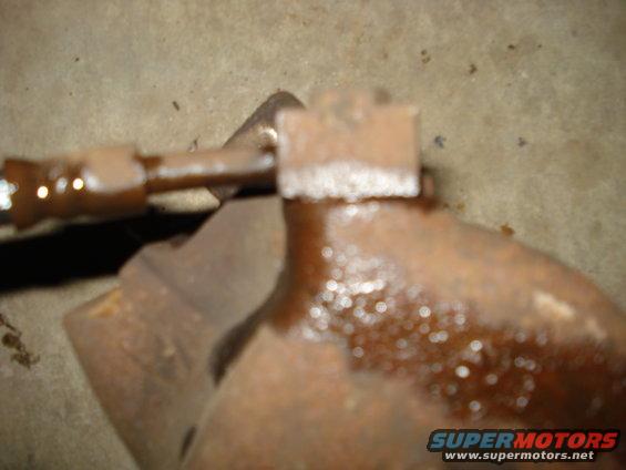 Close-up of a rusted brake caliper part with a metal line attached