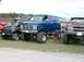 1994 Ford Bronco - Several modified vehicles, including a lifted blue GMC van, are displayed on a grassy field.