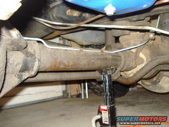 close-up of rusty rear axle and suspension components on a vehicle supported by a jack stand
