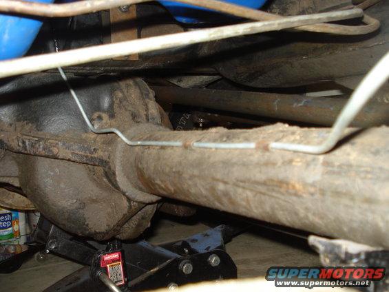 Underside view of a vehicle's rear axle, brake lines, and suspension parts supported by jack stands
