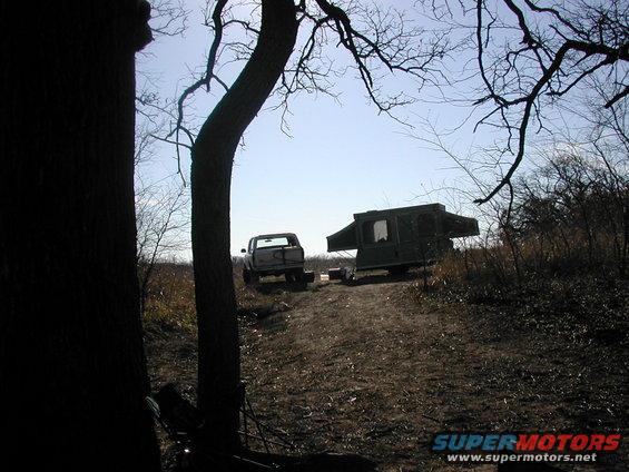 Truck with a pop-up camper attached, viewed from the rear on a dirt path