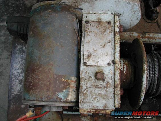 Close-up of a rusty winch, showing a Honeywell label on the motor housing and a steel cable wound on the drum